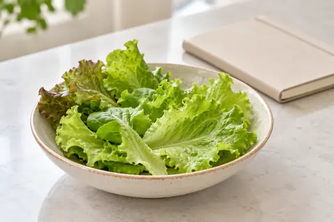 A few picked loose-leaf lettuce leaves in a small bowl on a kitchen counter; AI-generated illustration with no growing device